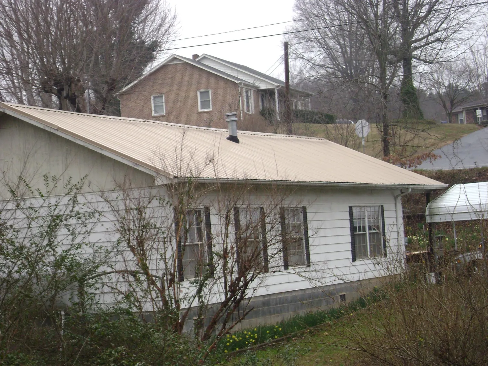 Tan metal roof on a white sided house set into a hillside — Commercial Roofing by Roofing Brothers in Kingsport